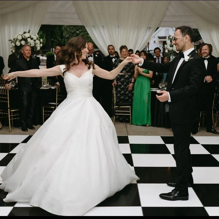 Bride and groom dancing on a checkered floor surrounded by their wedding party