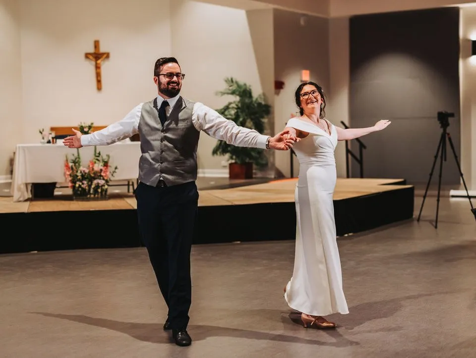 A father and bride open their arms to the room during the father–daughter dance