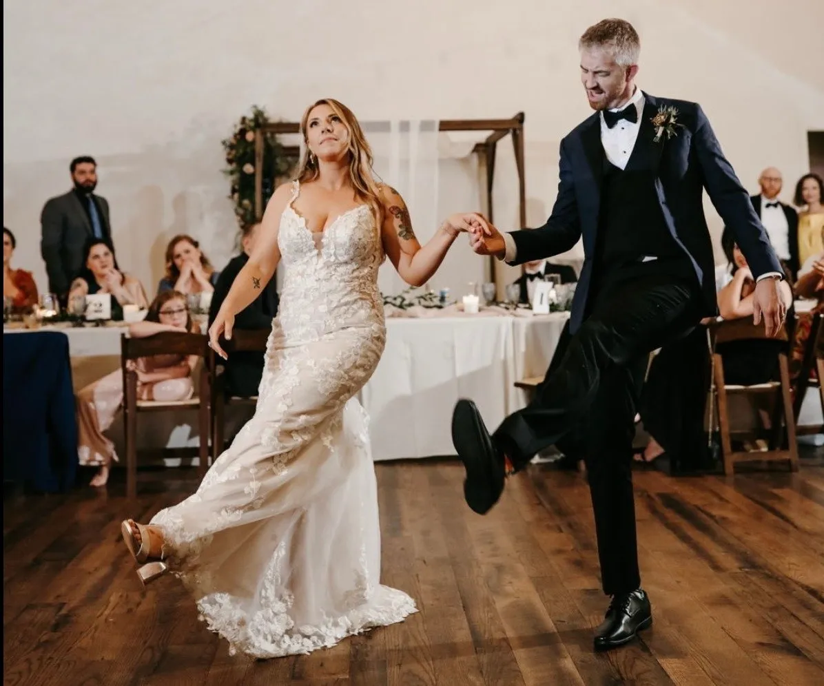 A couple laughing mid-step as wedding guests watch from their tables