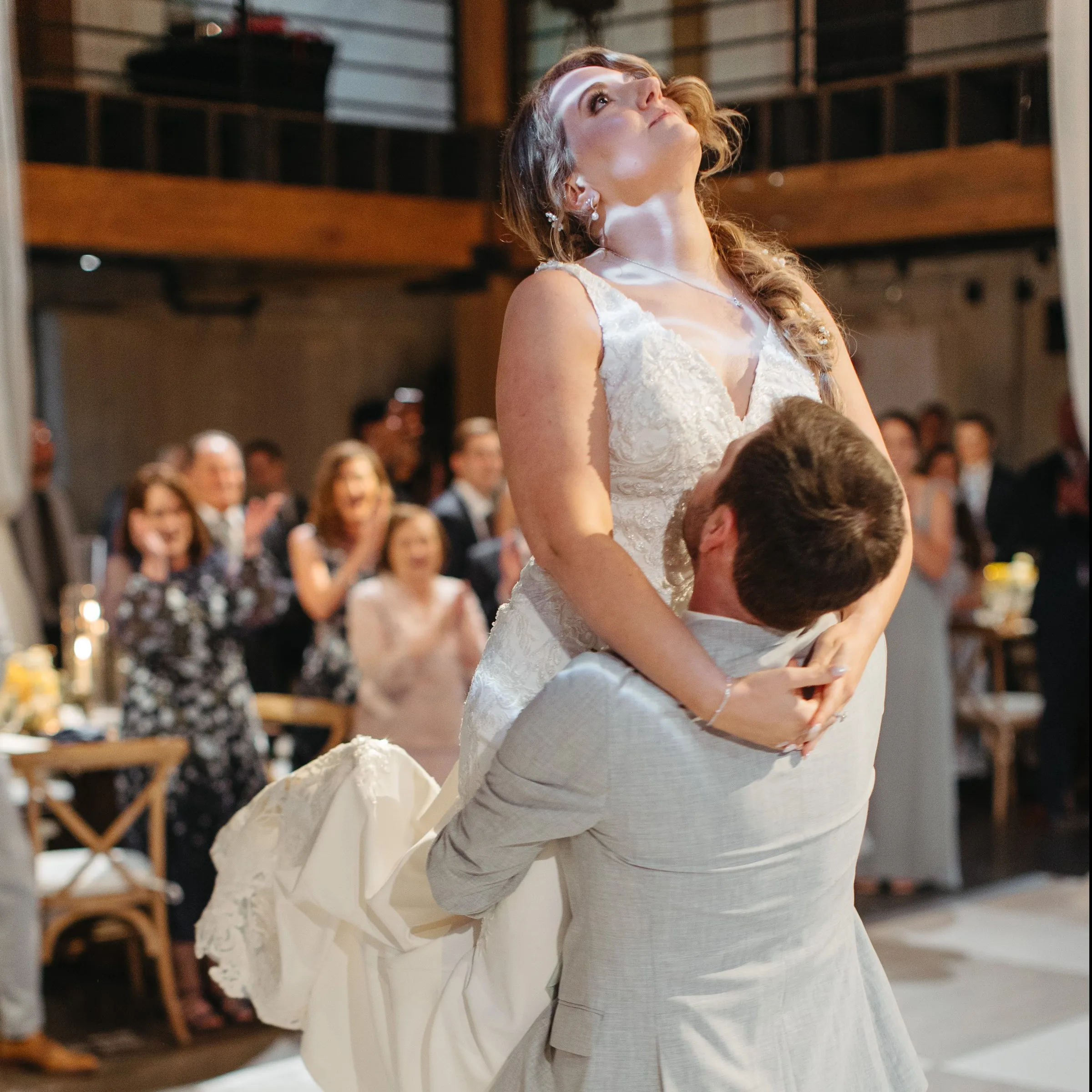 A groom lifts his bride as guests cheer from their tables
